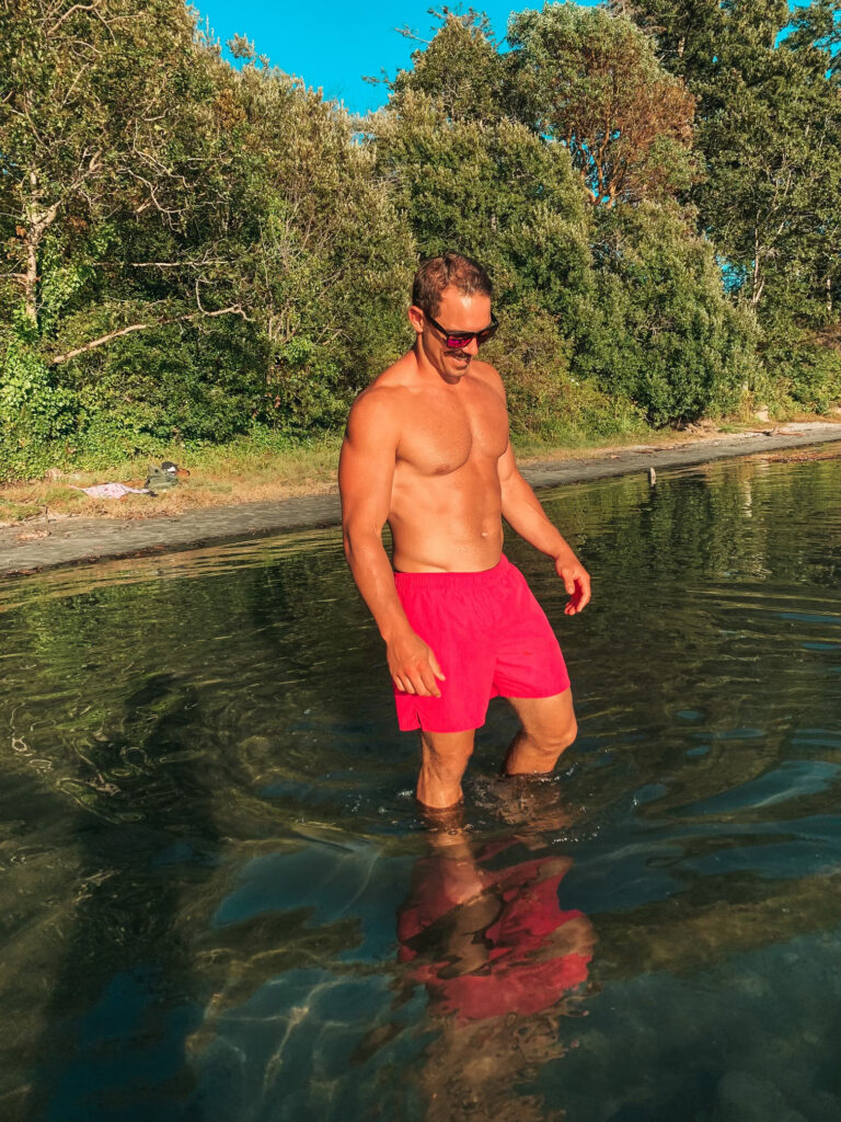 Brandon in pink shorts standing in the water in the summertime, looking down